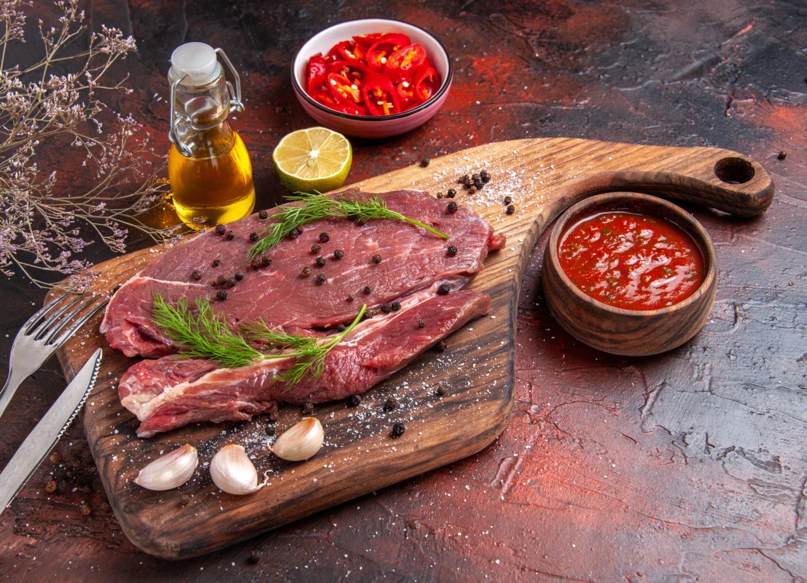 front-view-red-meat-wooden-cutting-board-garlic-green-pepper-fork-knife-dark-background
